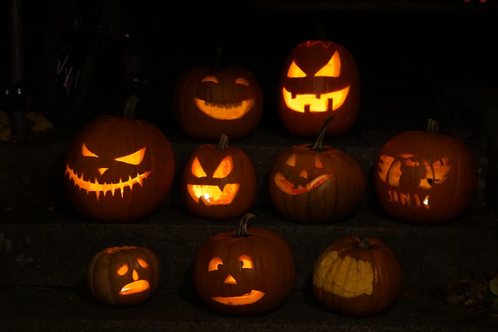 9 Halloweenkürbisse stehen im Dunkeln auf einer steinernen Treppe und zeigen ihre gruseligen Gesichter