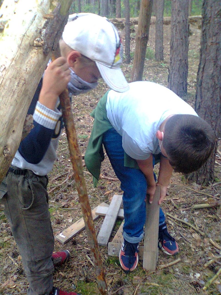 Zwei Jungen stehen im Wald und stecken einen Ast in die Erde