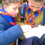 Zwei Jungen mit Pfadfinderhalstuch lesen in einem aufgeschlagenen Buch