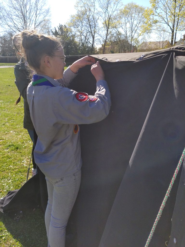 Eine Pfadfinderin knöpft eine schwarze Seitenplane ans Zelt.