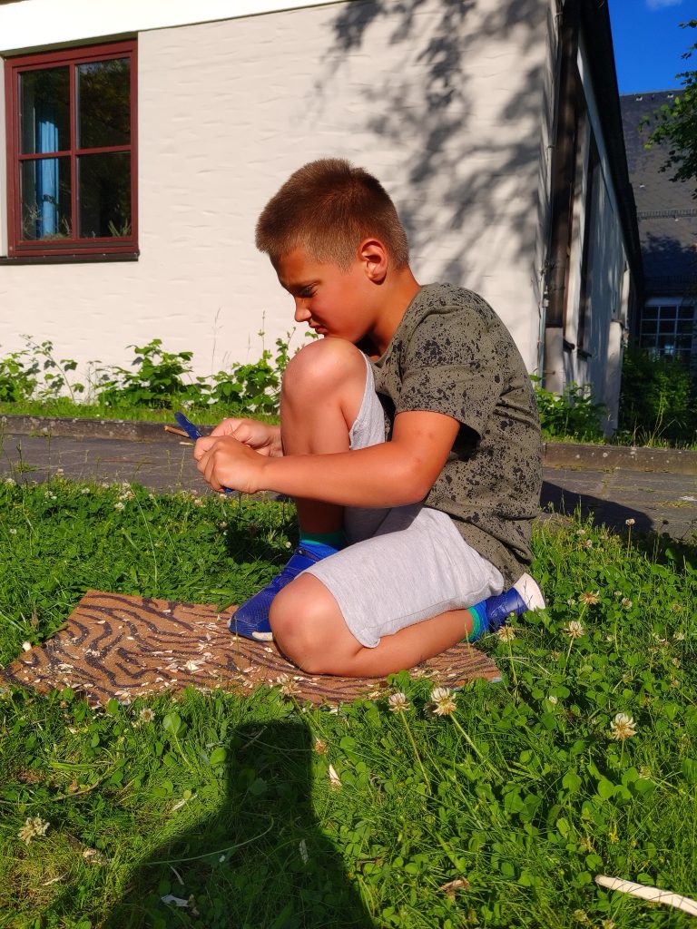 Ein Junge kniet in der Sonne und schnitzt.