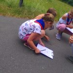 Drei Mädchen hocken auf dem asphaltierten Boden und begutachten ein verstorbenes Tier