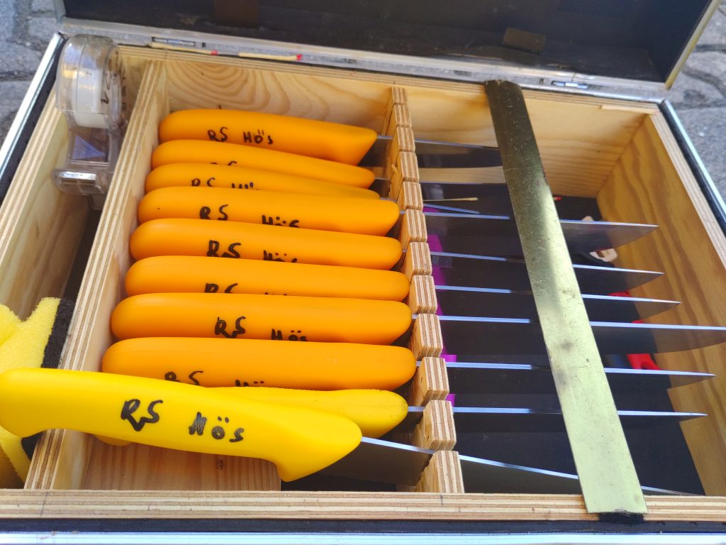 Ein Koffer mit gelben und organgen Messern. Auf allen Messern steht "Rvs Hös"